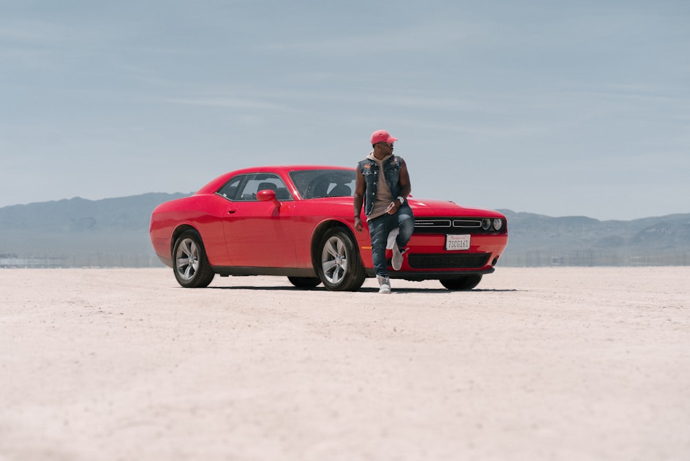 man in black jacket and black pants sitting on red car hood during daytime