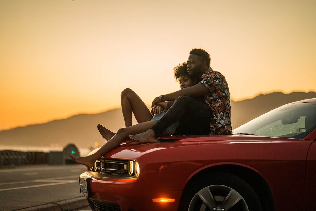 A couple sitting on a car bonnet