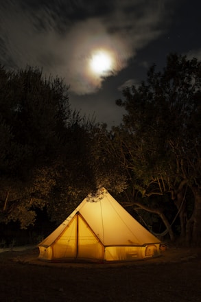A cozy glamping tent nestled among lush green trees with soft fairy lights glowing at dusk.