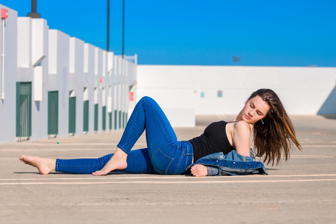 woman in black long sleeve shirt and blue denim jeans sitting on gray concrete floor during