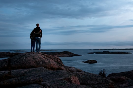 man in black jacket standing on brown rock formation near body of water during daytime in Kungshamn Sweden