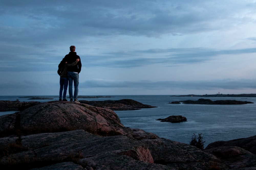 man in black jacket standing on brown rock formation near body of water during daytime