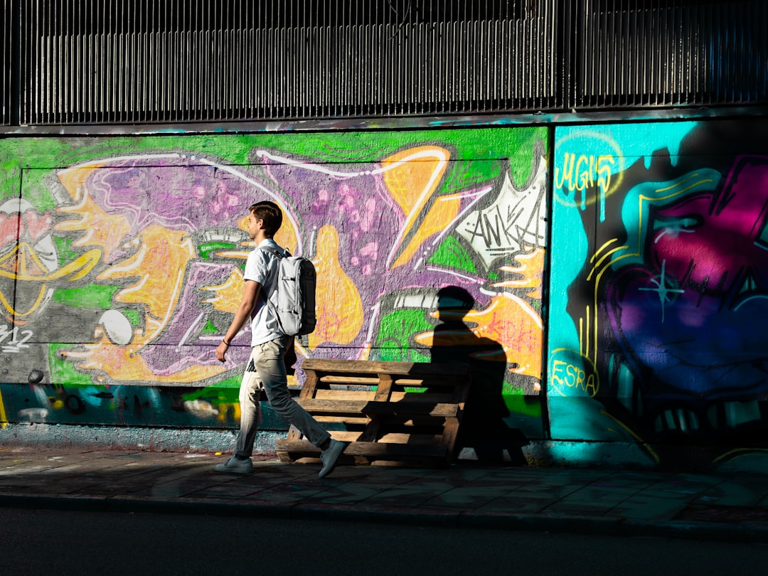 man in white shirt and black pants standing beside graffiti wall during daytime