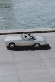 A sleek convertible cruising along a scenic coastal road in Europe with the top down.