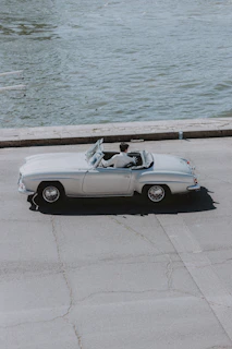 A classic convertible cruising along a coastal highway with the ocean in view