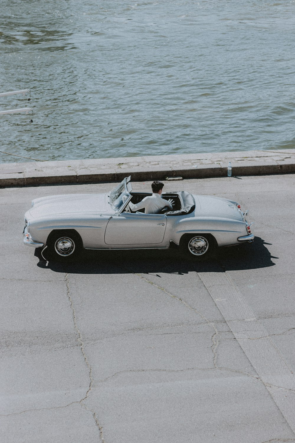 white convertible car parked on gray concrete pavement near body of water during daytime