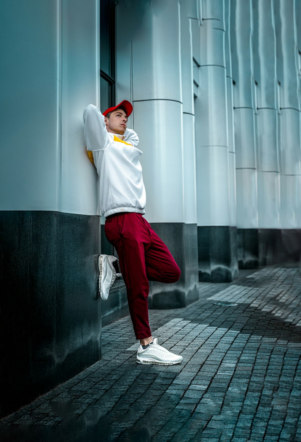 man in white long sleeve shirt and red pants leaning on wall