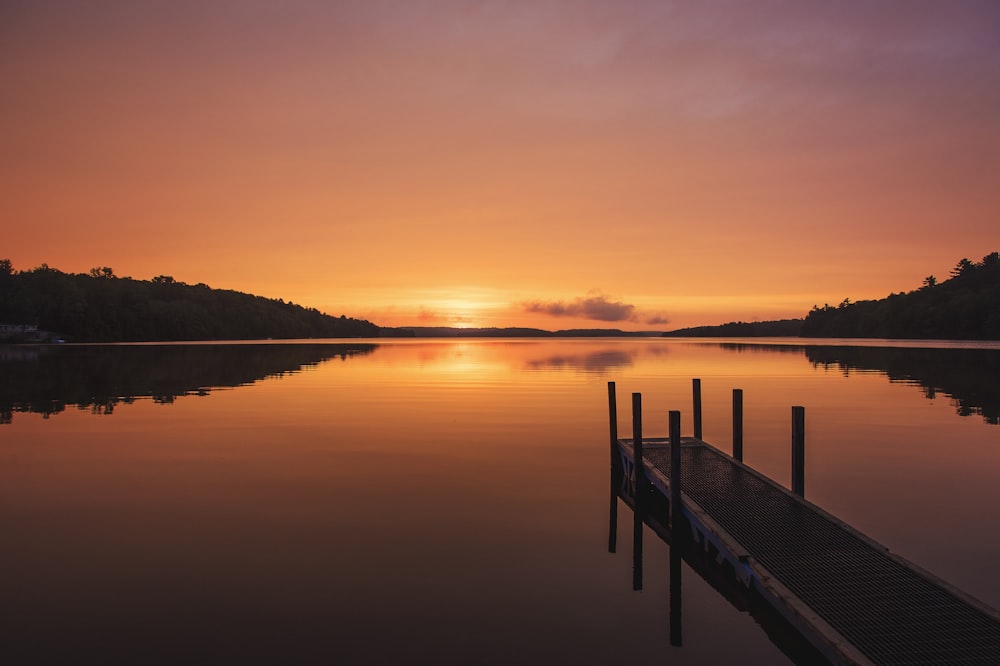 brown wooden dock on calm water during sunset