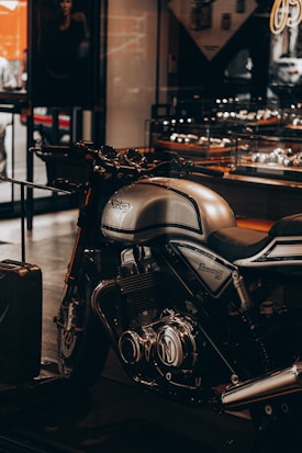 A sleek and polished Norton Commando 961 motorcycle is prominently displayed indoors. The bike features a metallic finish with chrome details and sits in a showroom or shop environment with various reflections visible on its surface. The overall ambiance suggests luxury and high performance.