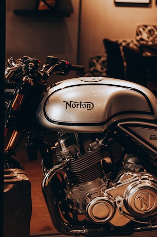 An artistic shot of a Norton motorcycle’s emblem shining against a backdrop of open road at dusk.