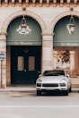 A luxury car is parked in front of the elegant facade of the Le Meurice building, characterized by two large arched windows and ornate lanterns. The building has a classic architectural style with stone columns.