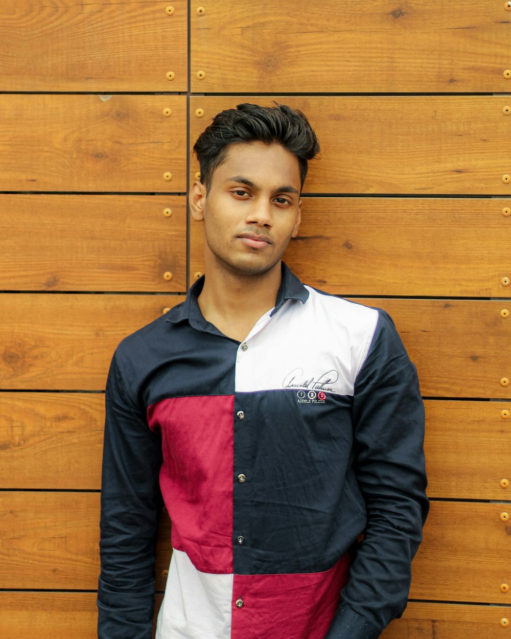 man in black and red zip up jacket standing beside brown wooden wall