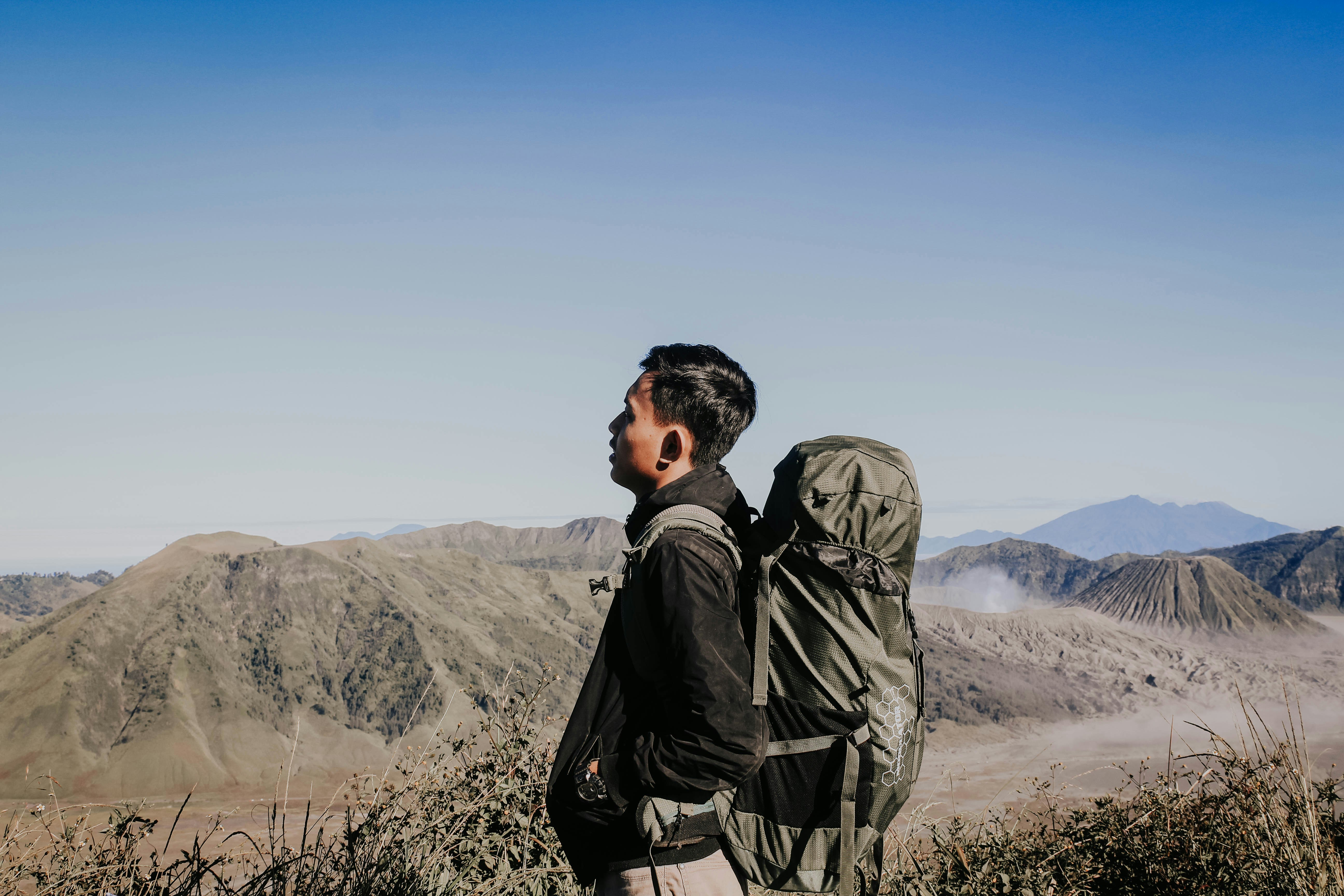 Traveler with backpack standing at scenic mountain overlook, bright sky, vast landscape below