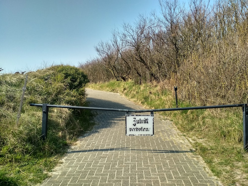 white and black road sign near green grass and trees under blue sky during daytime