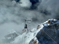 A cable car ascending towards a snowy mountain peak with hikers enjoying the view.