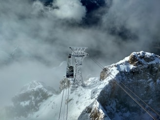 A cable car ascending towards a snowy mountain peak with hikers enjoying the view.