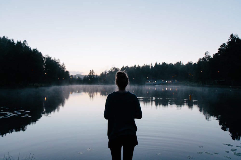 homme en veste noire debout près du lac pendant la journée