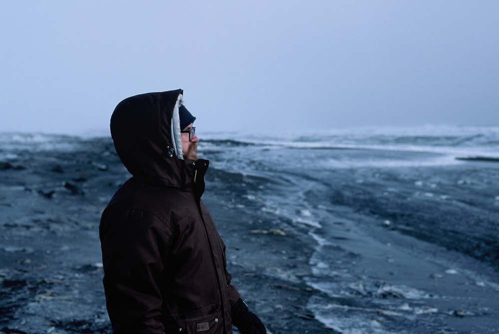 person in black hoodie standing on seashore during daytime