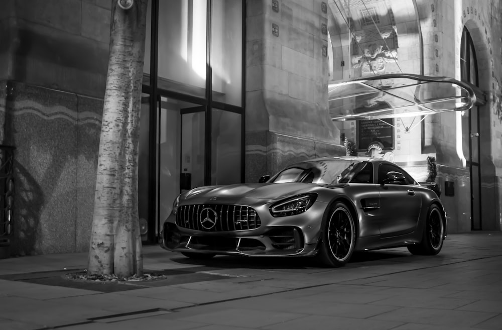 grayscale photo of mercedes benz coupe parked beside building