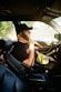 man in black t-shirt and brown hat driving car