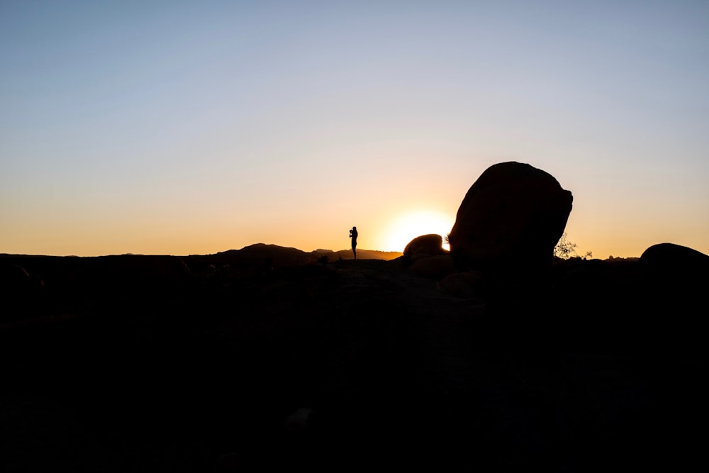 silhouette of person standing on rock during sunset