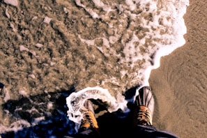 Short surf boots displayed on sandy beach with waves in background.