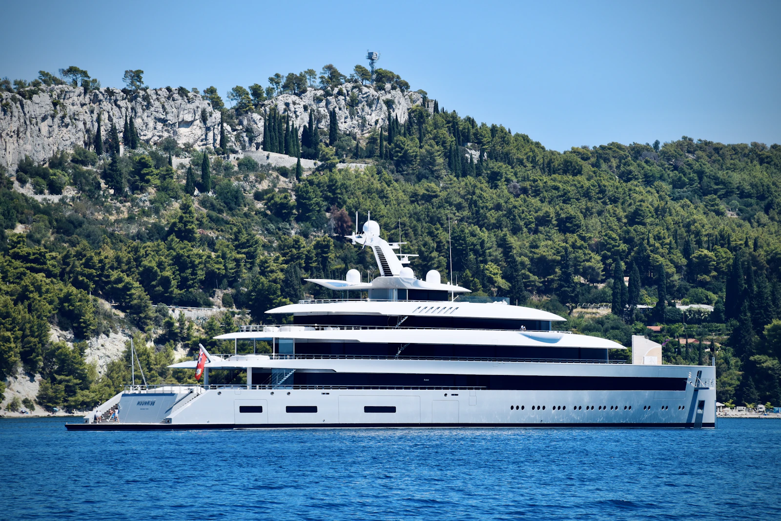 M/Y Nocturne — full side profile of the explorer superyacht along a pine-covered coast