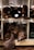 Multiple rolled-up sheets of leather are organized on wooden shelves. The leather is primarily dark brown, with some variably textured surfaces. The rolls are neatly arranged, showcasing a variety of leather types and thicknesses.
