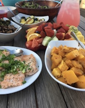 A colorful spread of dishes including pizza, salad, pasta, salmon, cake, and lemonade on a rustic wooden table.