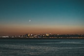 A serene crescent moon glowing above a mosque silhouette at dusk.