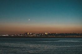 A serene crescent moon glowing above a mosque silhouette at dusk.