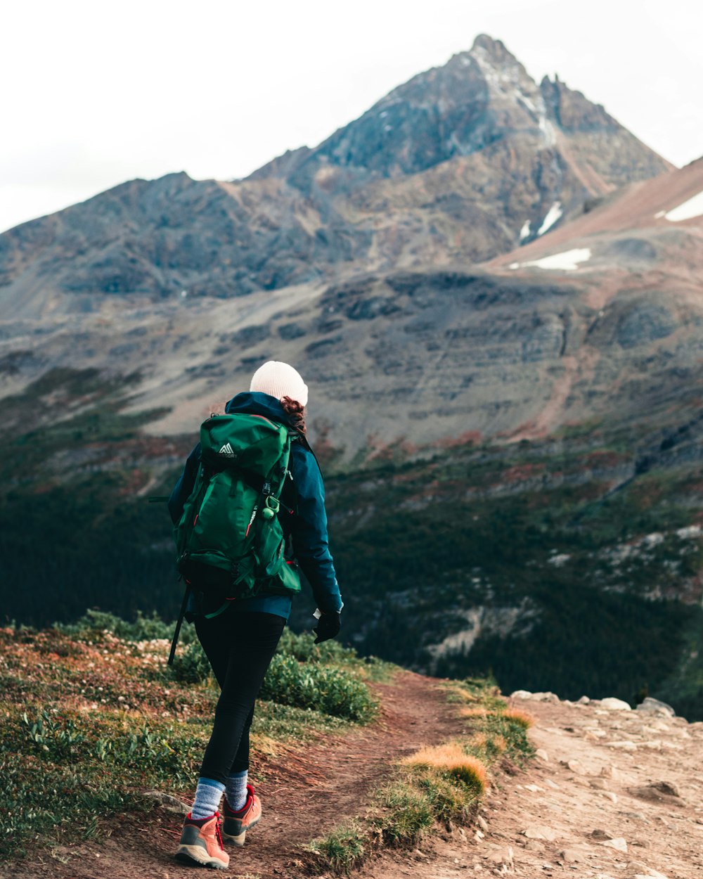 man in green jacket and black pants with backpack standing on brown rock mountain during daytime