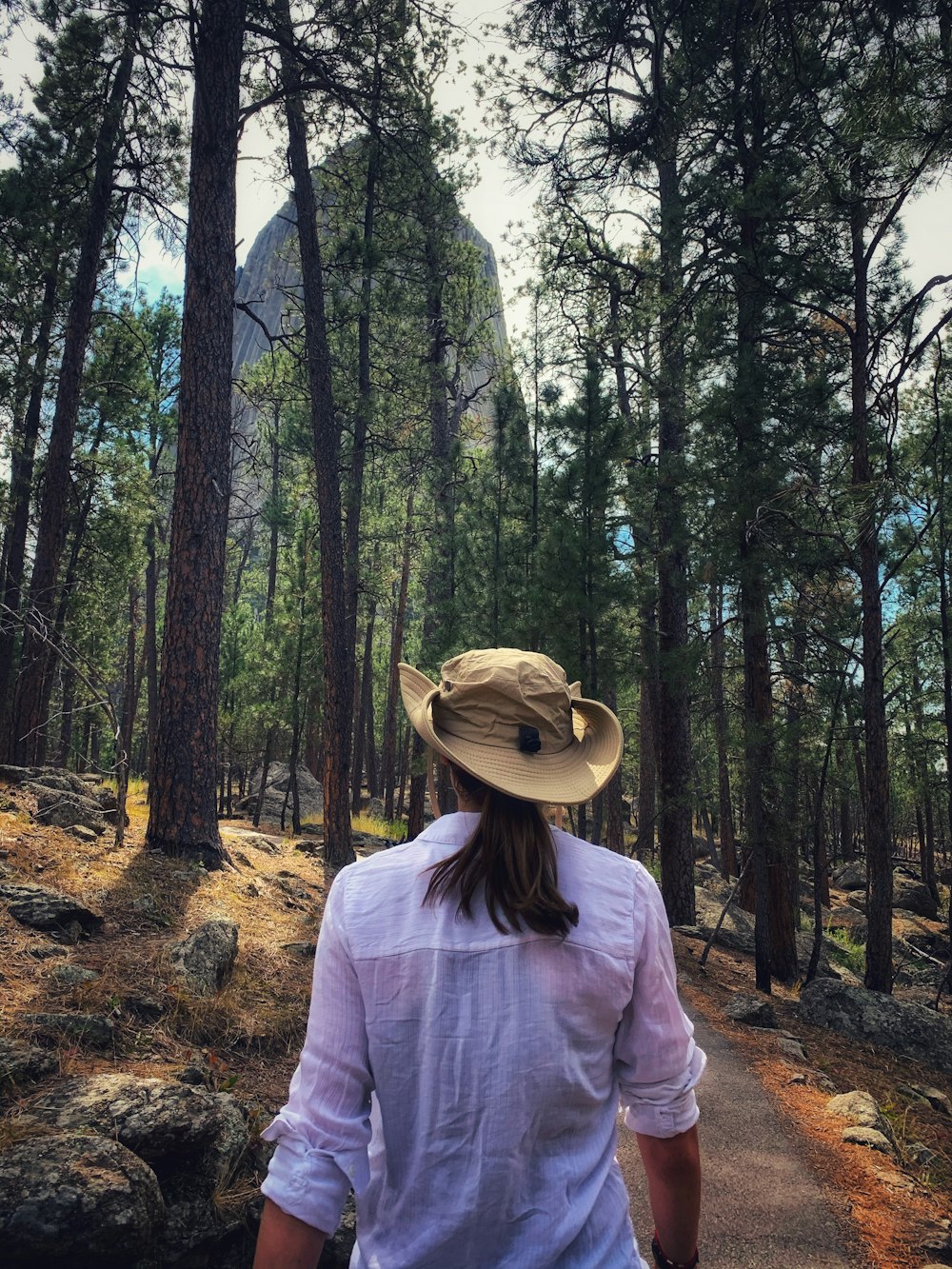 낮 동안 녹색 나무 근처에 서 있는 갈색 모자를 쓴 흰색 긴 소매 셔츠를 입은 여자