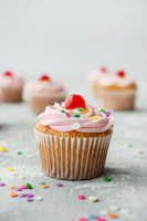 Close-up of a colorful cupcake topped with vibrant sprinkles and a glossy cherry.