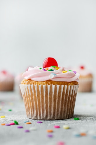 Close-up of a rustic wooden table displaying a variety of colorful cupcakes with pastel pink frosting and delicate sprinkles.