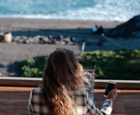 woman in white and black plaid shirt holding black smartphone