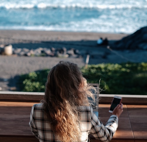 woman in white and black plaid shirt holding black smartphone