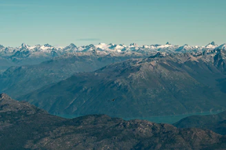 A vast mountain range under a clear blue sky with a lone eagle soaring.