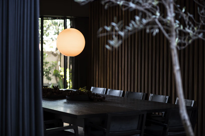 A cozy dining room softly lit by a farmhouse wooden pendant over a rustic wooden table.