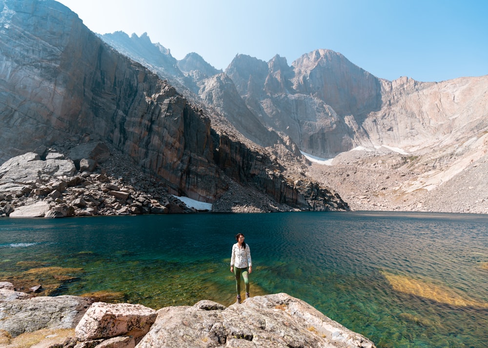 Uomo in camicia bianca in piedi sulla roccia vicino al lago durante il giorno