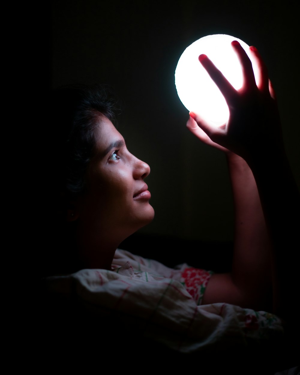 woman in white and red floral shirt holding white light bulb