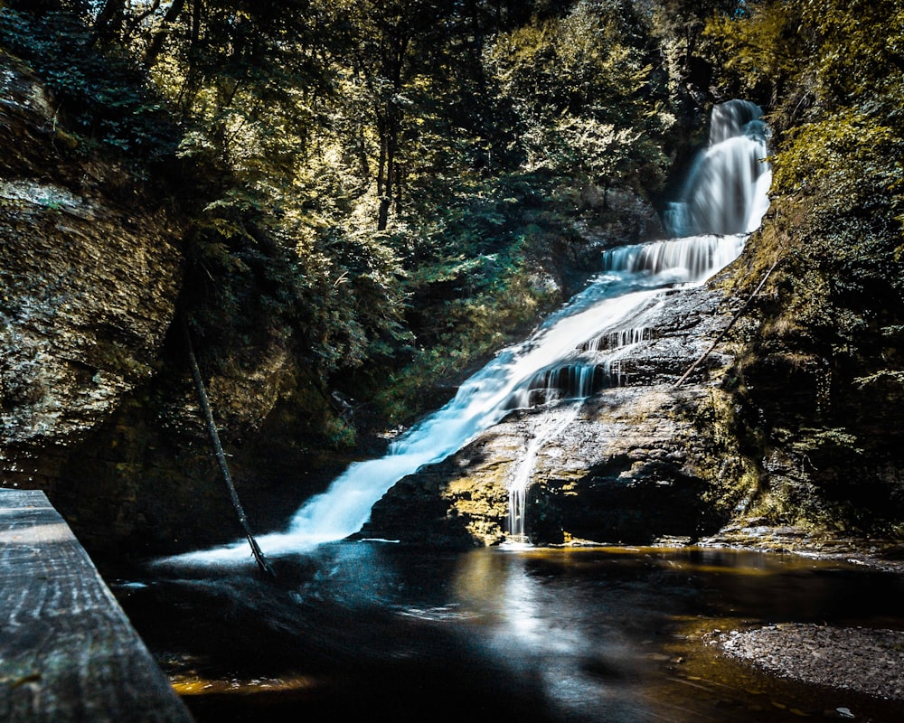 man in white hoodie standing on rock formation in front of waterfalls during daytime