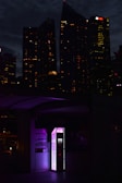 A vibrant city street at night featuring loginexus smart lockers glowing with neon purple and blue hues.