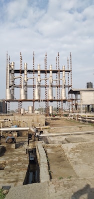 An industrial site with multiple tall, cylindrical metal structures and piping systems. The structures are elevated on a framework of girders. The ground appears to be a concrete platform with additional piping and ducts. The sky above is partly cloudy.