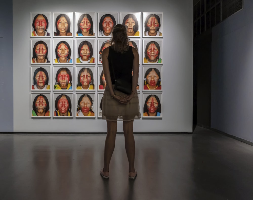 woman in black tank top and brown shorts standing in front of assorted paintings