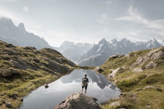 Hiker resting by a crystal-clear mountain lagoon surrounded by lush greenery.