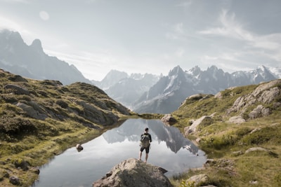 Hiker resting by a crystal-clear mountain lagoon surrounded by lush greenery.