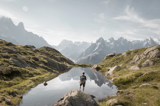 Hiker pausing to admire a serene mountain lake at dawn, with mist rising gently.