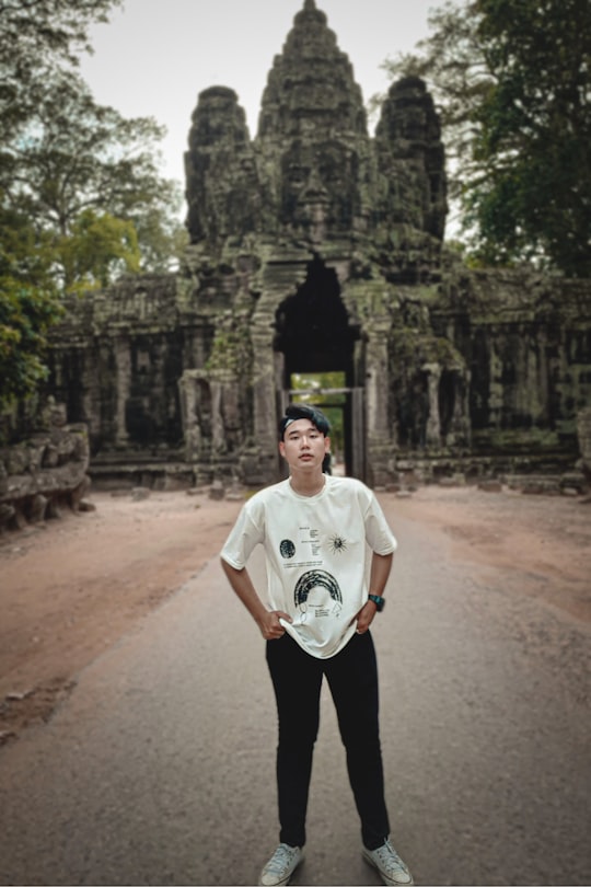 man in white crew neck t-shirt and black pants standing on brown dirt road during in Angkor Thom Cambodia