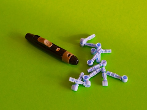 A black and beige lancing device is placed on a bright green surface alongside multiple blue and white lancets scattered around.